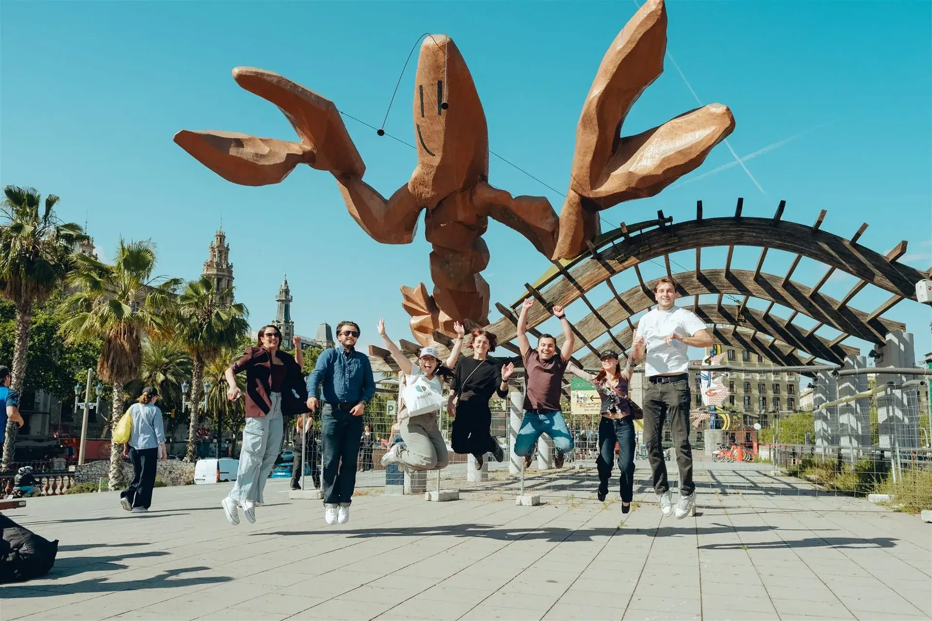 A team jumping for joy beneath a giant sculpture on the Barcelona waterfront